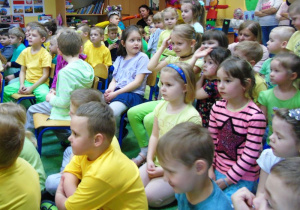 Dzieci siedzą na dywanie i oglądają przedstawienie.