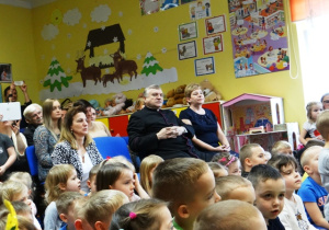 Duża grupa dzieci siedzi na dywanie i ogląda występ koleżanek i kolegów.