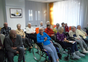 Osoby starsze siedzą i oglądają występ dzieci.