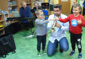 Dwóch chłopców stoi obok muzyka i naciskają klawisze w instrumencie.
