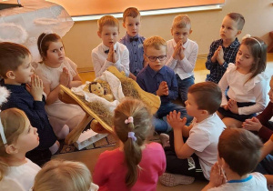 Dzieci siedzą na dywanie i śpiewają.