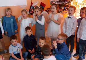 Dzieci stoją obok choinki i śpiewają.