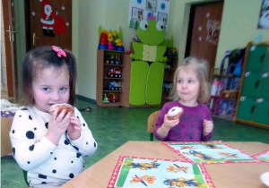 Dzieci siedzą przy stoliku i jedzą pączki.