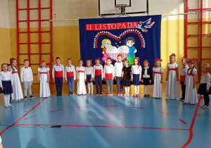 Występujące dzieci stoją w półkolu i śpiewają piosenkę.
