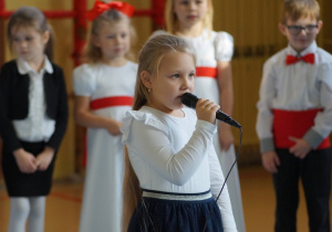 Dziewczynka trzyma mikrofon i mówi wiersz.