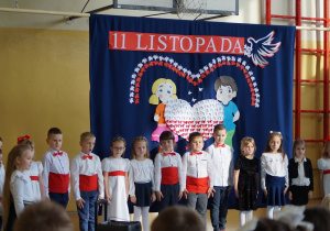 Dzieci ustawione na scenie stoją na baczność.
