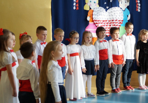 Dzieci występujące na scenie śpiewają piosenkę.
