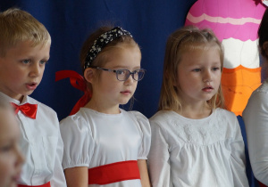 Chłopiec i dwie dziewczynki na scenie śpiewają piosenkę.