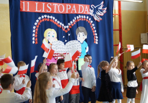 Występujące dzieci machają chorągiewkami.