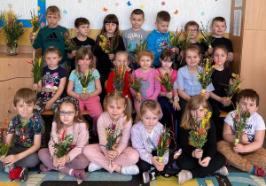 Grupa dzieci pozuje do zdjęcia trzymając w dłoniach wykonane przez siebiepalmy wielkanocne.