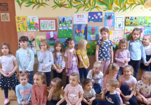 Grupa dzieci pozuje do zdjęcia. W tle wystawa prac.