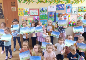 Grupa dzieci pozuje do zdjęcia z dyplomami. W tle wystawa prac.