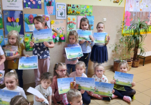 Grupa dzieci pozuje do zdjęcia z dyplomami. W tle wystawa prac.