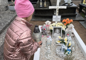 Dziewczynka kładzie znicz na grobie