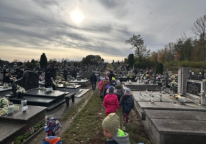 Grupa dzieci idzie w parach przez cmentarz