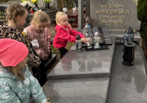 Dziewczynka kładzie znicz na grobie obok niej stoją trzy dziewczynki