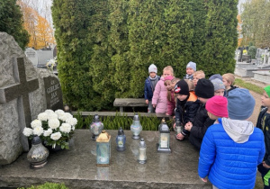 Chłopczyknkładzie znicz na grobie obok niego stoi grupa dzieci