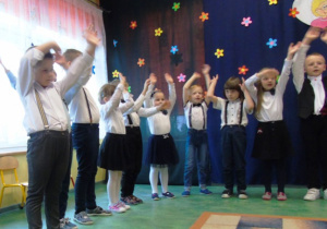 Dzieci odświętnie ubrane trzymają rączki w górze