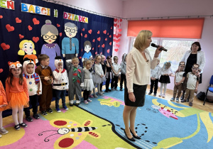 Pani Dyrektor przemawia do publiczności. Za nią stoją występujące dzieci.