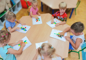 Dzieci siedzą przy stoliku tworząc pracę plastyczną na temat dowolny.
