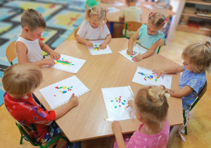 Cztery dziewczynki i dwóch chłopców tworzą pracę plastyczną przy stoliku