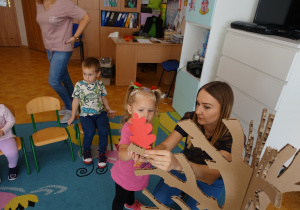 Dziewczynka z opiekunką zawieszająca na papierowym drzewie ozdobiony przez siebie liść