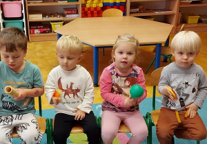 Przedszkolaki siedzące na krzesełkach, trzymające instrumenty muzyczne