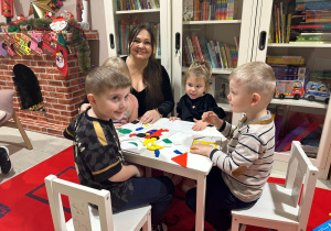 Przedszkolaki siedzące przy stoliku z opiekunem w trakcie zajęć