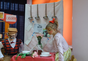 Dziewczynka przebrana za babcię i chłopiec przebrany za dziadka na tle dekoracji z PRL-u