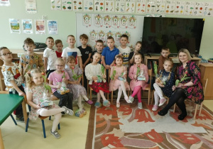Dziewczynki wraz z opiekunką trzymające w rękach tulipany, za nimi grupa chłopców