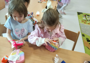 Dziewczynki odpakowujące przy stolikach otrzymane prezenty