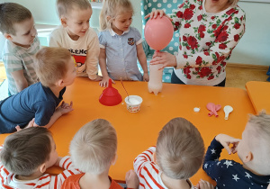 Przedszkolaki przygotowujące eksperyment z balonem pod opieką nauczycielki.