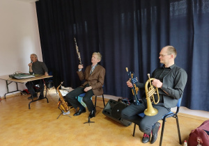 Muzycy filharmonii prezentujący saksofon i trąbki.