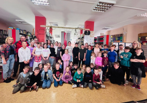 Grupa przedszkolaków wraz z uczniami i nauczycielami w szkolnej bibliotece.