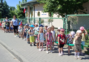 Grupa przedszkolaków idąca chodnikiem parami wraz z opiekunkami.