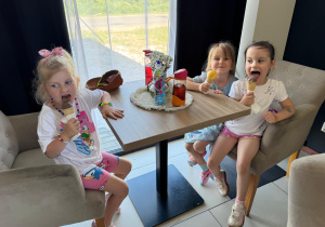 Trzy dziewczynki jedzące lody przy stoliku w restauracji.