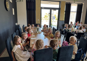 Grupa przedszkolaków siedząca przy stolikach i jedząca lody w restauracji.