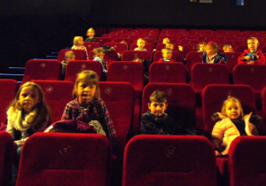 Dzieci siedzą na sali kinowej.