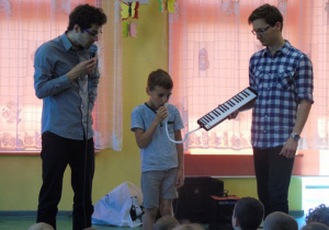 Chłopiec gra na melodyce a przy nim stoi dwóch mężczyzn