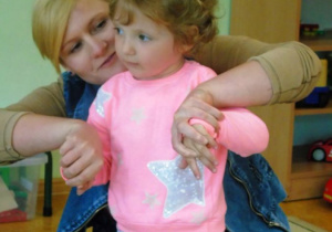 Kobieta tzryma za rączki małą dziewczynkę w różowej bluzeczce
