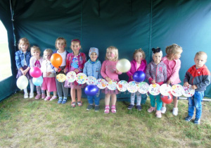 Dzieci stoją i tzymają balony i kolorowe talerzyki papierowe własnoręcznie ozdobione