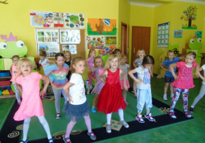 Grupa dziewczynek stoi na dywanie wykonkonuje ruch taneczne