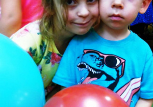 Chłopiec z dziewczynką stoją i trzymają kolorowe balony.