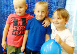Trzej chłopcy stoją obok siedzie i trzymają niebieskie balony.