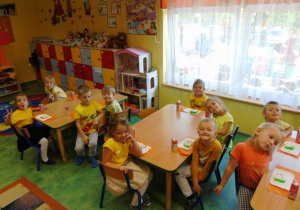 Dzieci ubrane w żółte koszulki sedzą przy stolikach i jedzą tort.