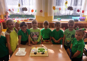 Dzieci ubrane w zielone koszulki patrzą na tort na którm narysowana jest żaba.