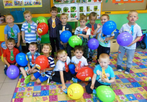 Dzieci siedzą i stoją na dywanie.Trzymają kolorowe balony.