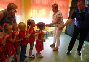 Kobieta pasuje dzieci ołówkiem na przedszkolaka przy niej stoi mężczyzna