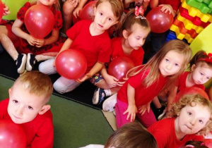 Dzieci w czerwonych koszulkach siedzą z balonami
