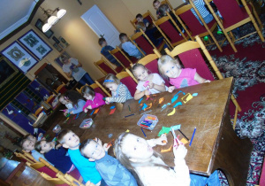 Dzieci siedza przy stole i wycinają.
